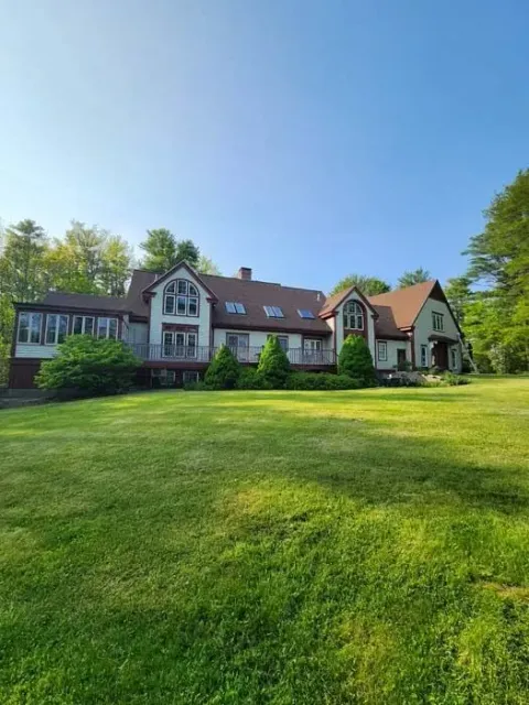Large white house with red roof beside a green lawn under a clear blue sky
