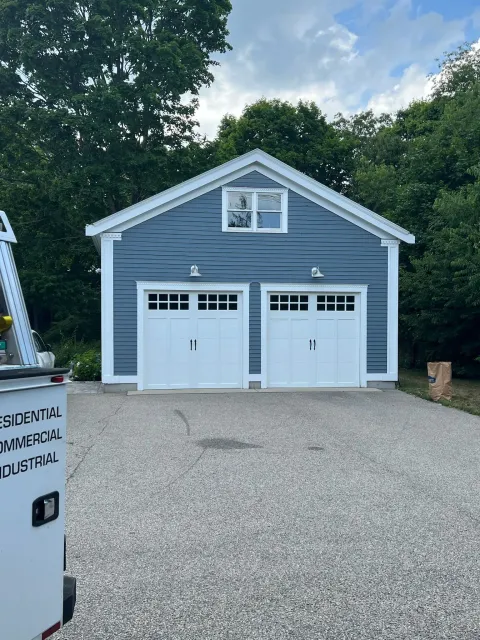 A blue garage with white doors and a white trailer parked in front of it.