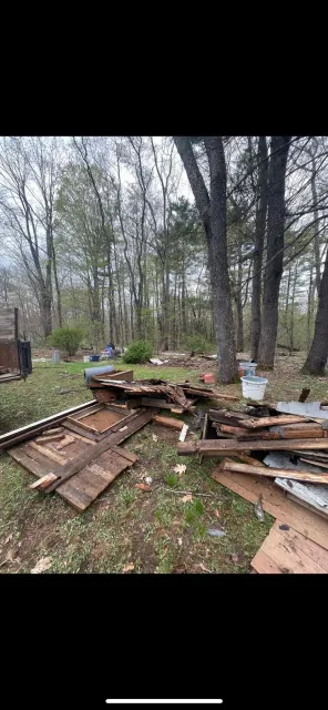 Debris and wood scraps from a dismantled structure scattered on the ground in a wooded area.