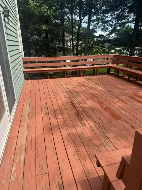 A red wooden deck with a bench and trees in the background.
