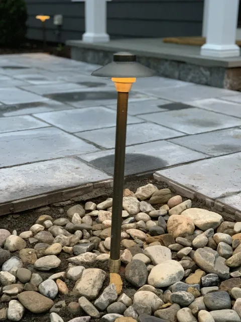 Small black garden path light glowing among river rocks beside a stone patio