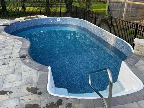 A large swimming pool is sitting on top of a patio next to a fence.