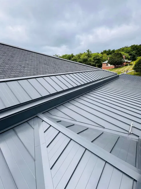Gray metal roof with standing-seam panels and cloudy sky in the background