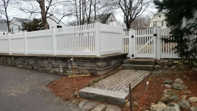 A white picket fence surrounds a stone wall and a stone walkway.