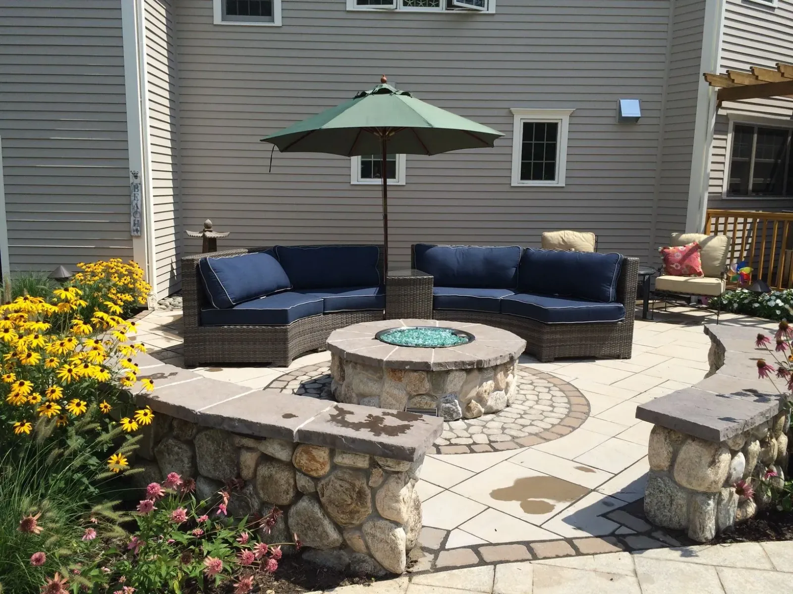 A patio with a fire pit surrounded by furniture and an umbrella