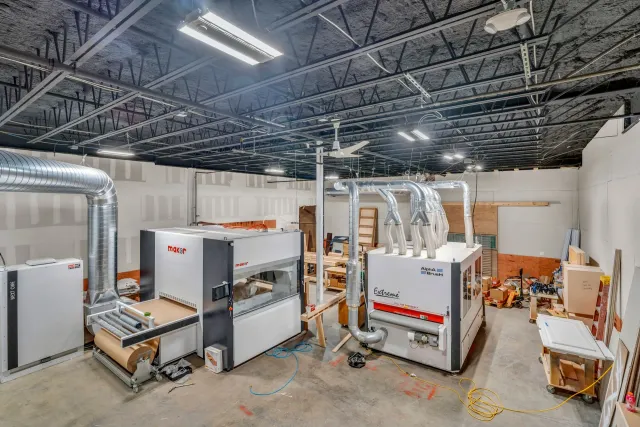 Two large industrial wood sanding machines with overhead ventilation ducts inside a warehouse workshop.