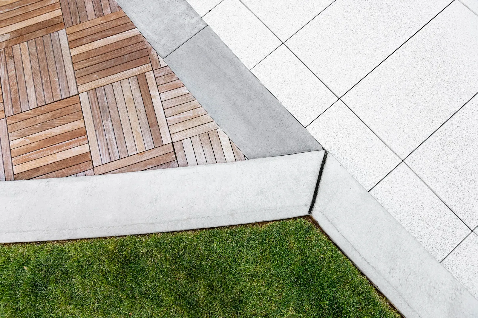 Modern landscape design featuring clean-cut lawn turf, wooden deck tiles, and sleek stone pavers — expert hardscaping and turf installation by Xquisite Landscaping in Massachusetts.