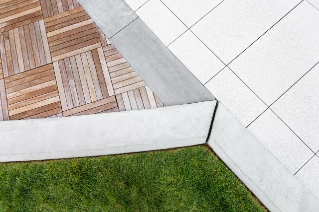 Modern landscape design featuring clean-cut lawn turf, wooden deck tiles, and sleek stone pavers — expert hardscaping and turf installation by Xquisite Landscaping in Massachusetts.