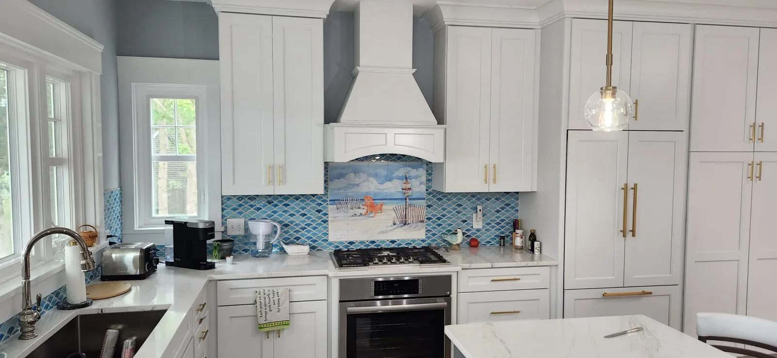 Modern kitchen with white cabinets, a blue tile backsplash, stainless steel appliances, and a decorative beach-themed tile mural over the stove.