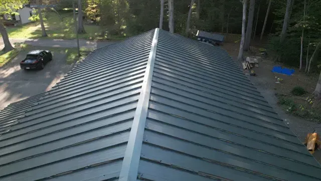 View from a roof ridge with green metal panels, overlooking a wooded driveway and parked car below