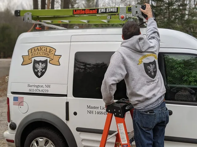 A Daigle Electric technician unloading a ladder from the company service van, which carries the Daigle Electric shield logo and NH master license number 14684.