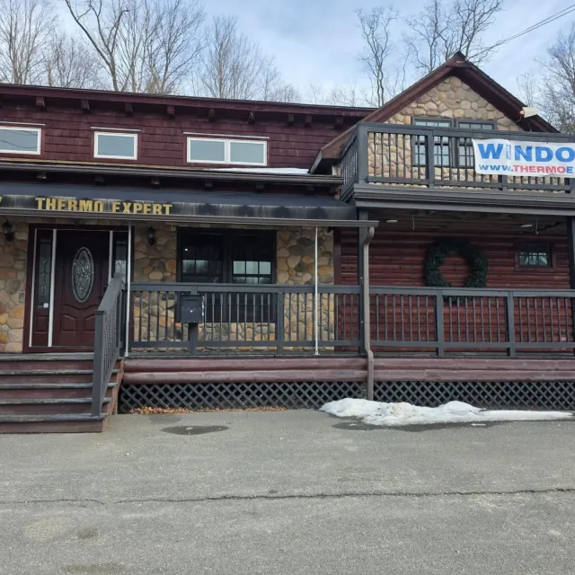 Log cabin storefront with porch railing and signs for The Thermo Expert and WNDO Windows, seen from the street