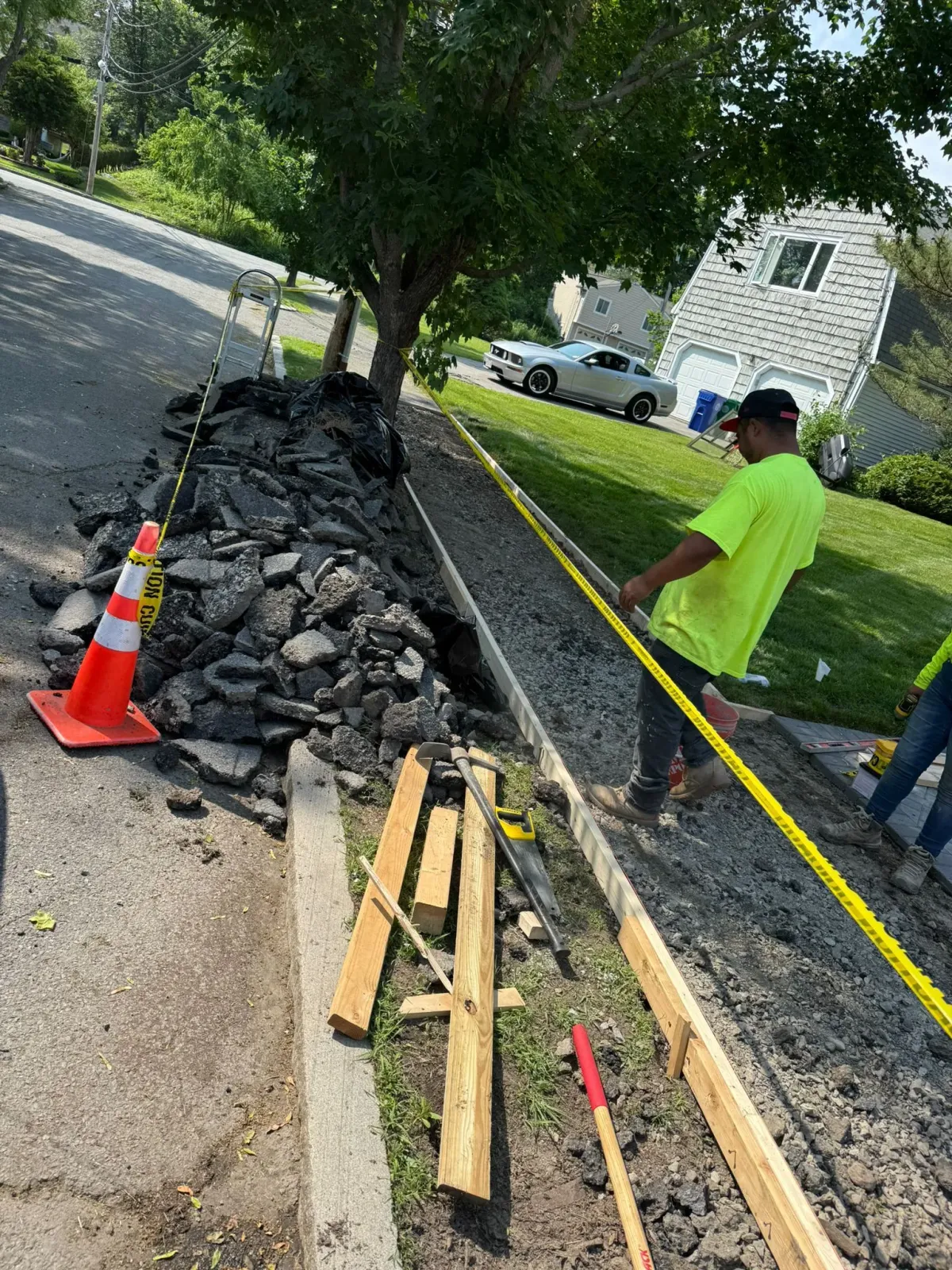 Workers constructing a concrete curb next to a road, using caution tape and tools.