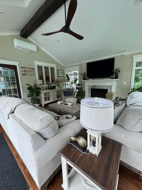 Bright living room with gray sofas, a fireplace, wall TV, and vaulted ceiling with a ceiling fan.