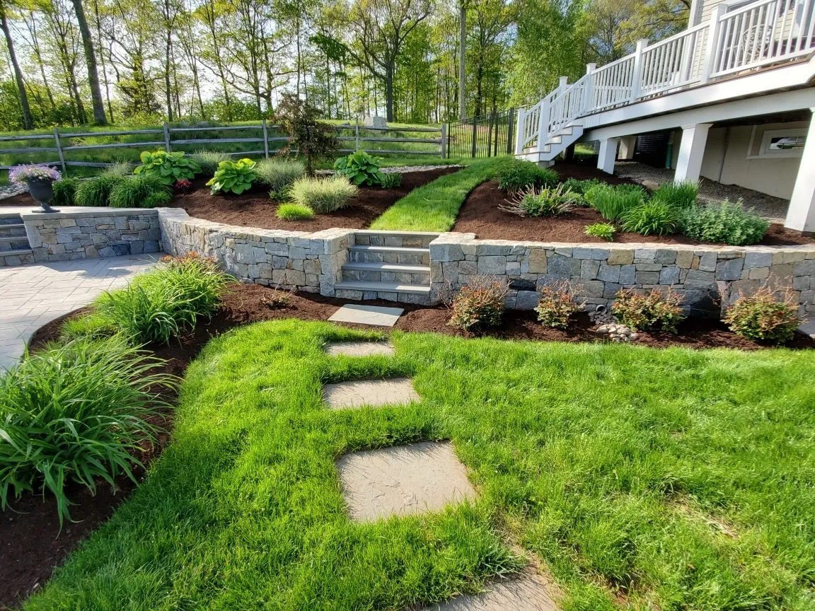 Beautiful backyard with retaining walls, stone walkway and steps, and fresh mulch, demonstrating the range of premium hardscaping and landscaping services offered by Keith Isham