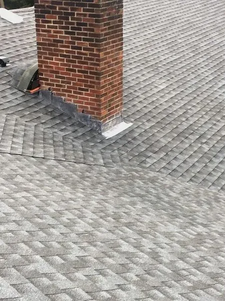 Brick chimney on a gray shingle roof, with flashing visible.