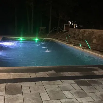 A large swimming pool is lit up at night with green lights.