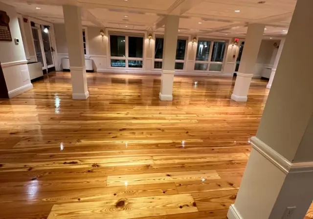 Spacious empty ballroom featuring polished light wood floors, white support columns, and large windows.