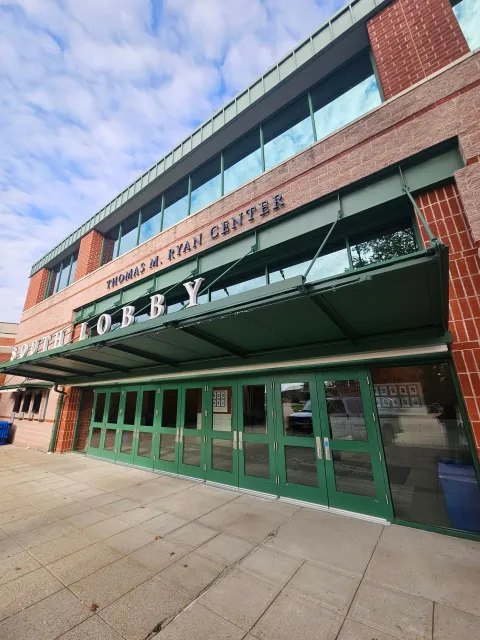 Tommy N. Ryan Center entrance with green doors and awning, brick facade, and blue sky.