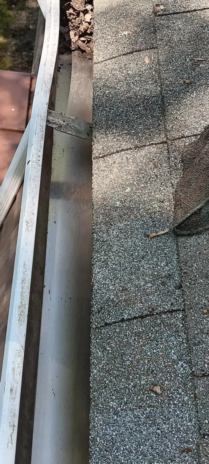 Close-up of a gravel roof edge with a white gutter and red shingles visible on the left