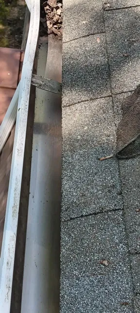 Close-up of a gravel roof edge with a white gutter and red shingles visible on the left