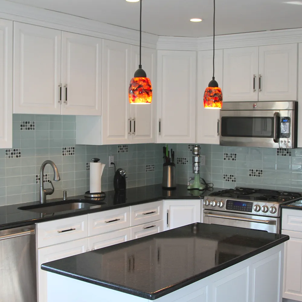 Modern kitchen with white cabinets, black countertops, light blue tile backsplash, and colorful pendant lights.