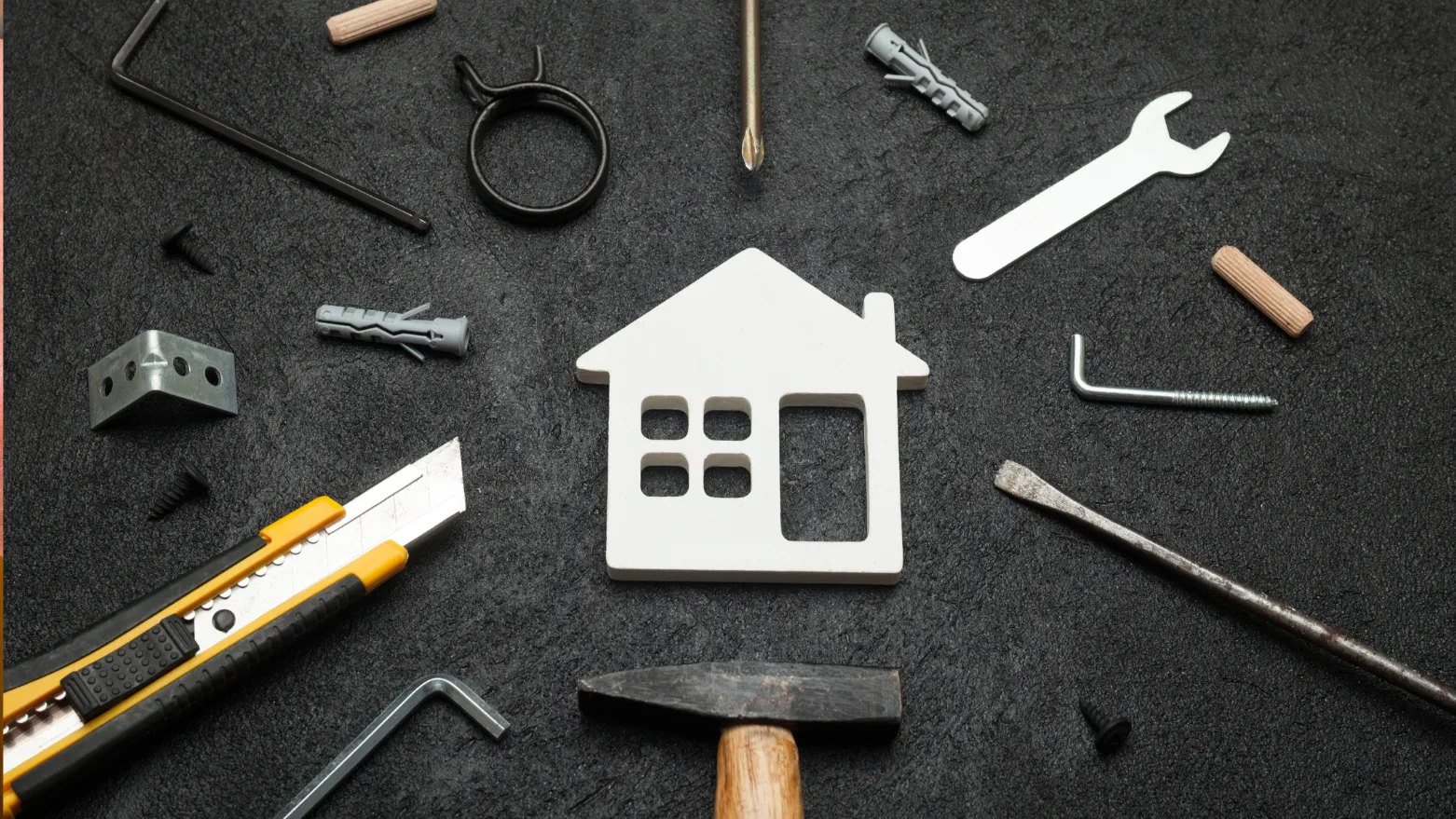 House-shaped cutout surrounded by construction tools and hardware on a black surface.