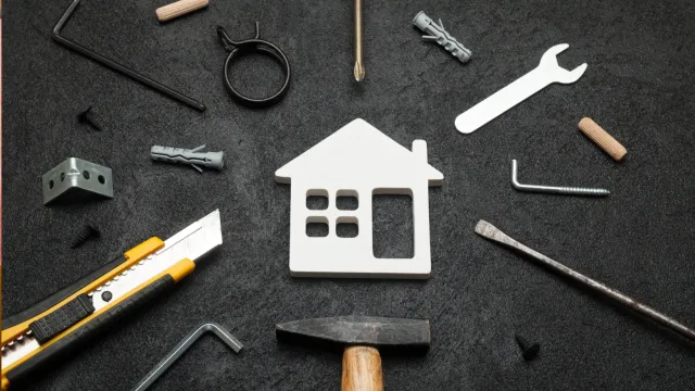 House-shaped cutout surrounded by construction tools and hardware on a black surface.