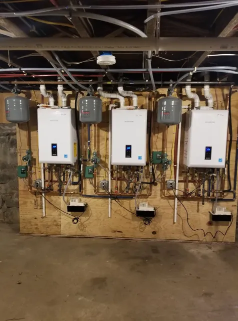 A row of water heaters are lined up on a wall in a basement.