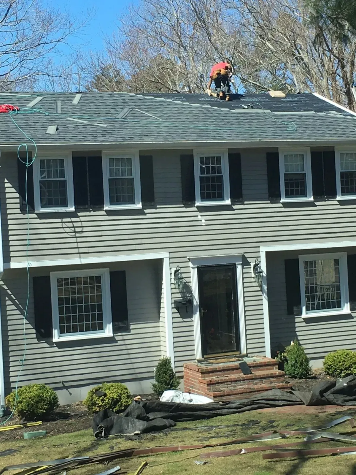 House with gray siding; a worker on the roof.