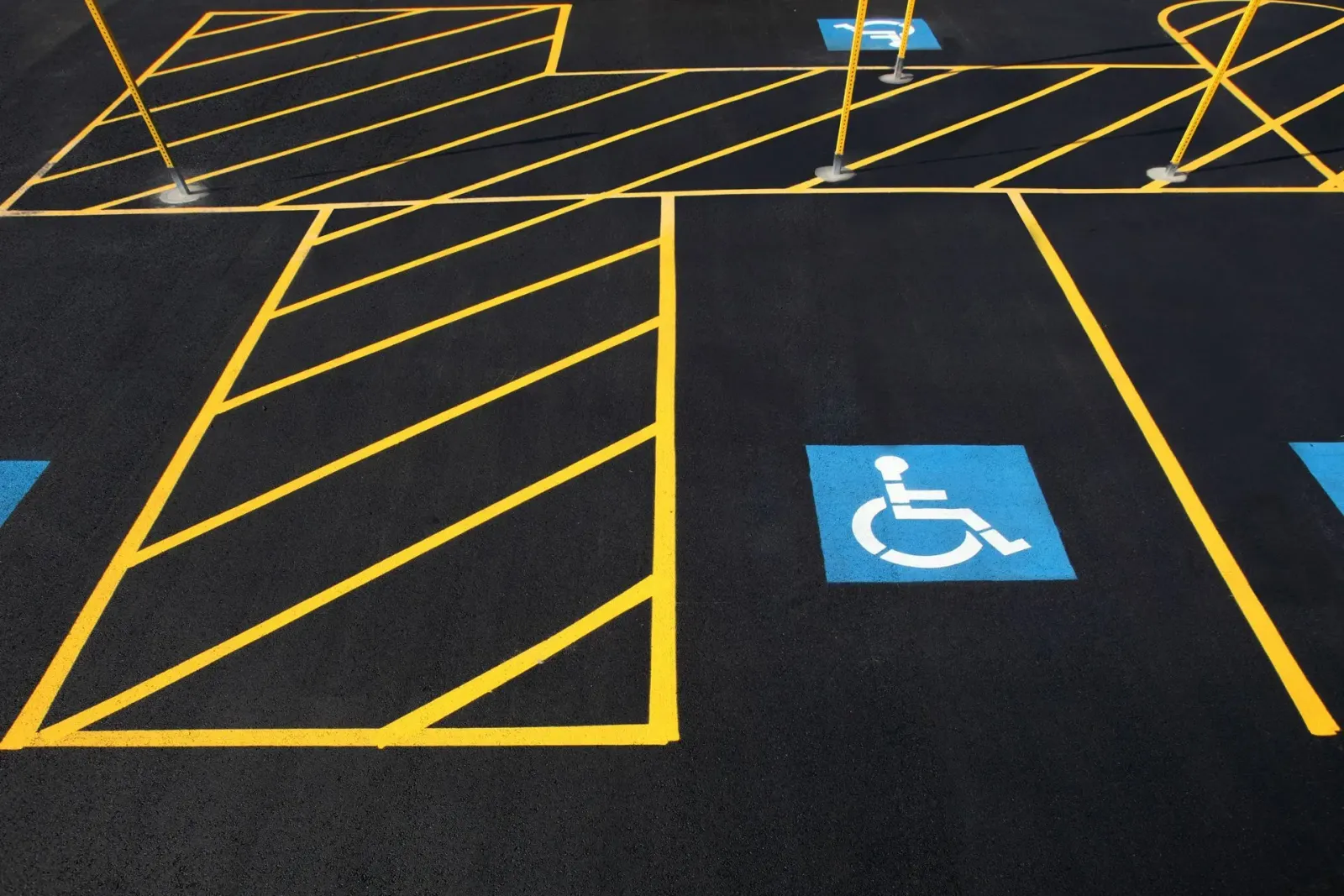 A freshly painted asphalt parking lot featuring a blue handicap parking symbol and yellow striped safety markings.