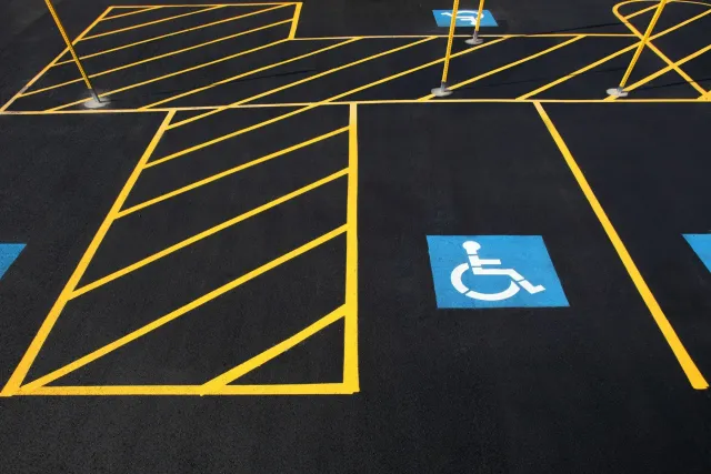 A freshly painted asphalt parking lot featuring a blue handicap parking symbol and yellow striped safety markings.