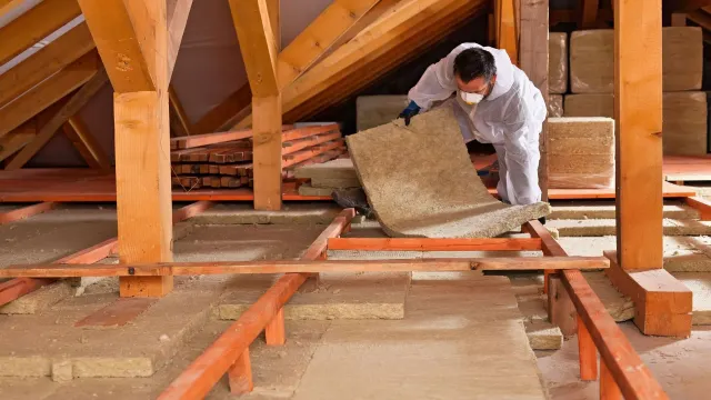 A man is laying insulation in the attic of a house.
