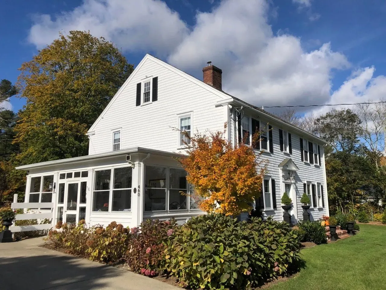 White house with screened porch, autumn foliage, blue sky.