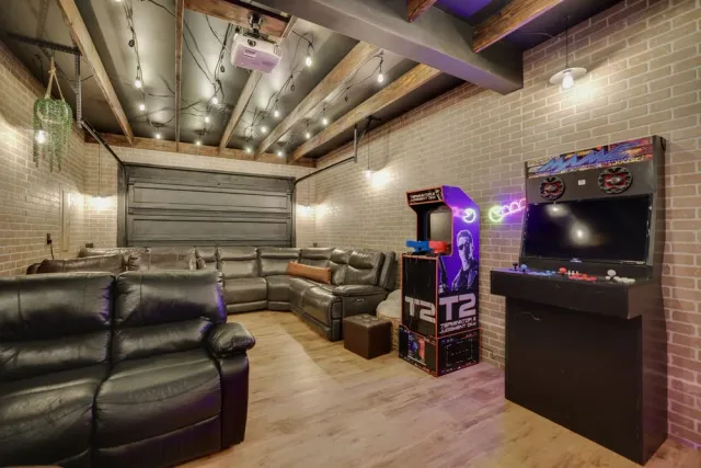 Game room with exposed wood beams, brick walls, string lights and arcade machines