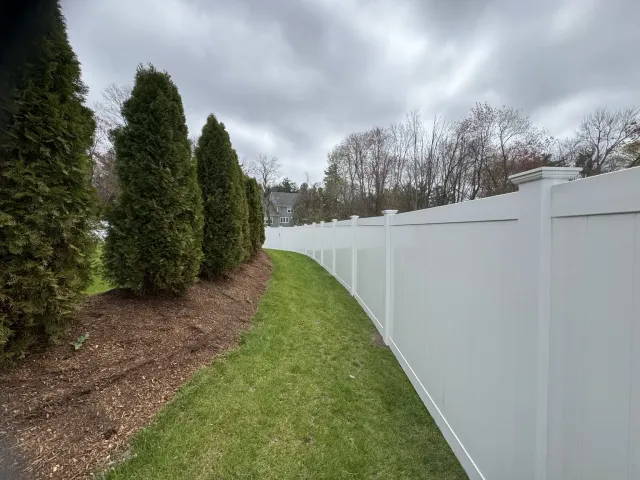 White vinyl privacy fence installed along a landscaped Massachusetts property