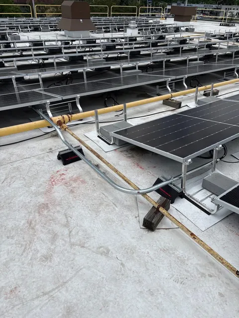 Galvanized conduit routed around a gas line between rows of rooftop solar panels