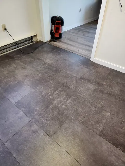 Dark gray stone-look flooring in a room transition, featuring a partially installed floor and a corner heater unit.