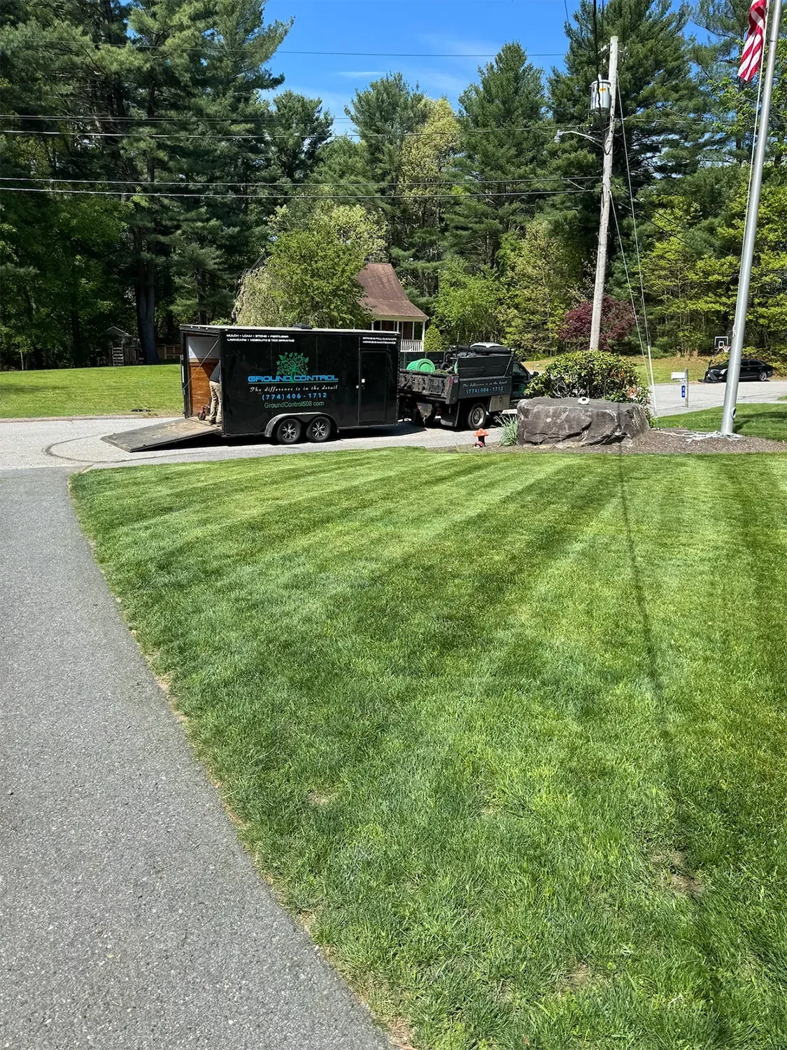 Trailer and debris near a well-manicured lawn with fresh mowing stripes; sunny day.
