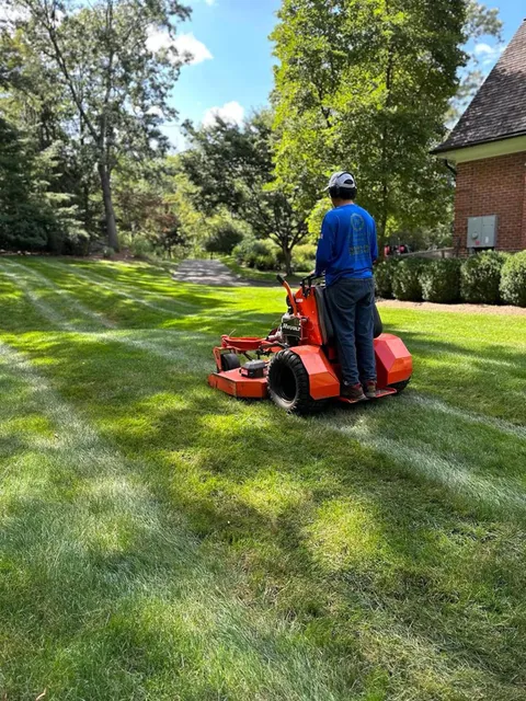 A man is riding a lawn mower on a lush green lawn.
