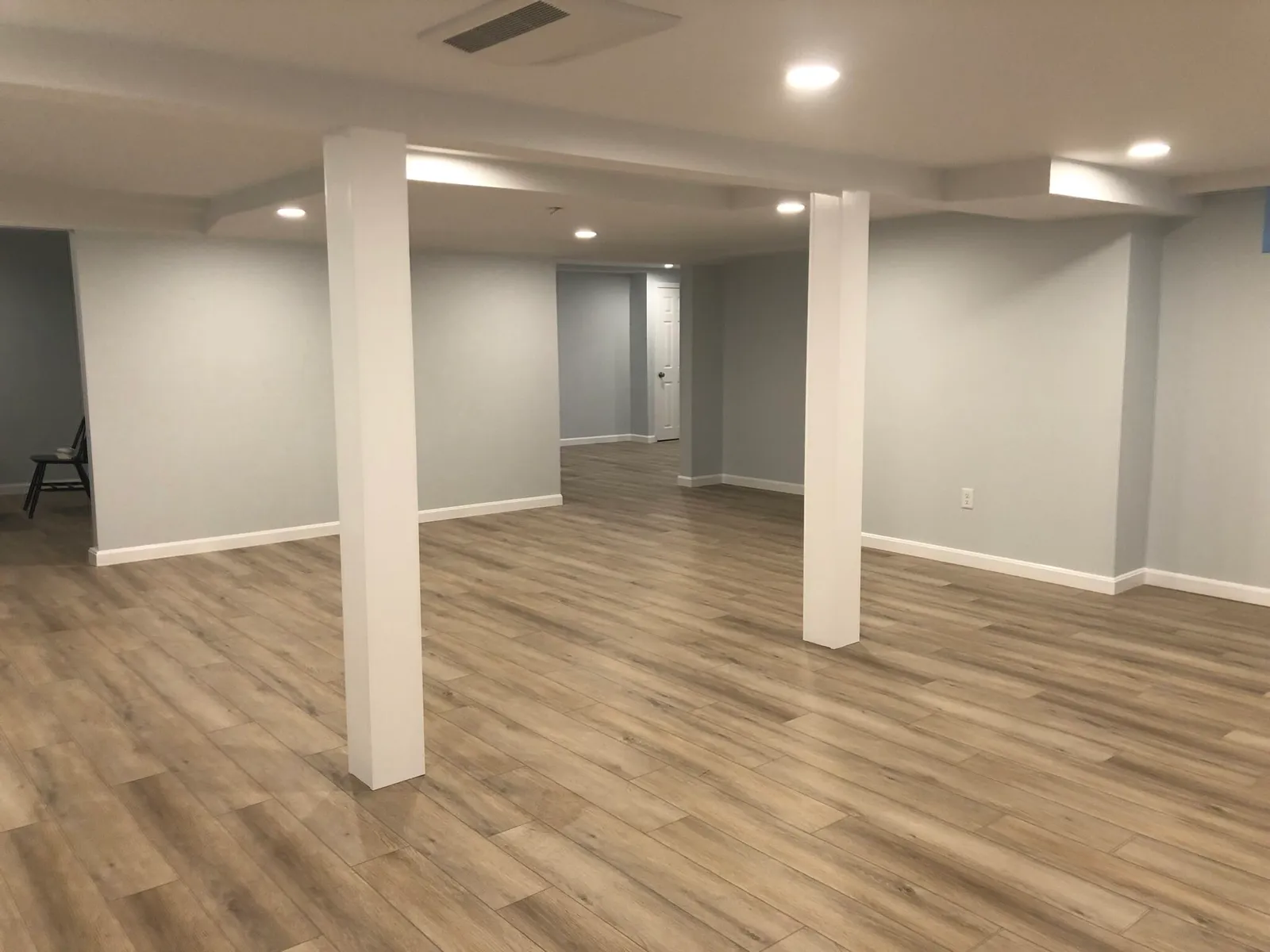 Finished basement with wood-look flooring, recessed lighting and painted support columns