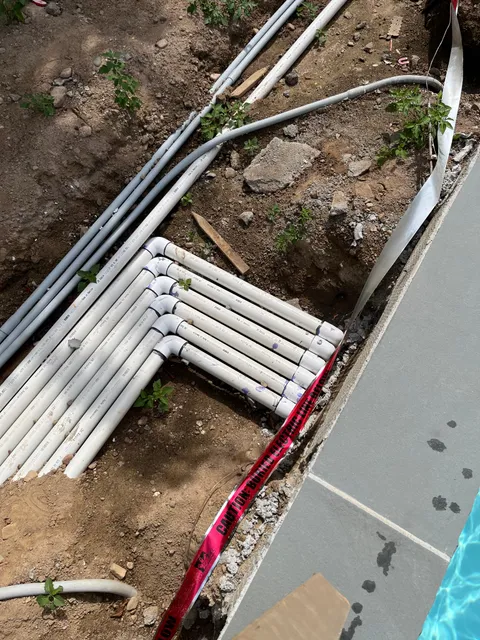 New PVC pool plumbing manifold installed alongside pool deck during repair