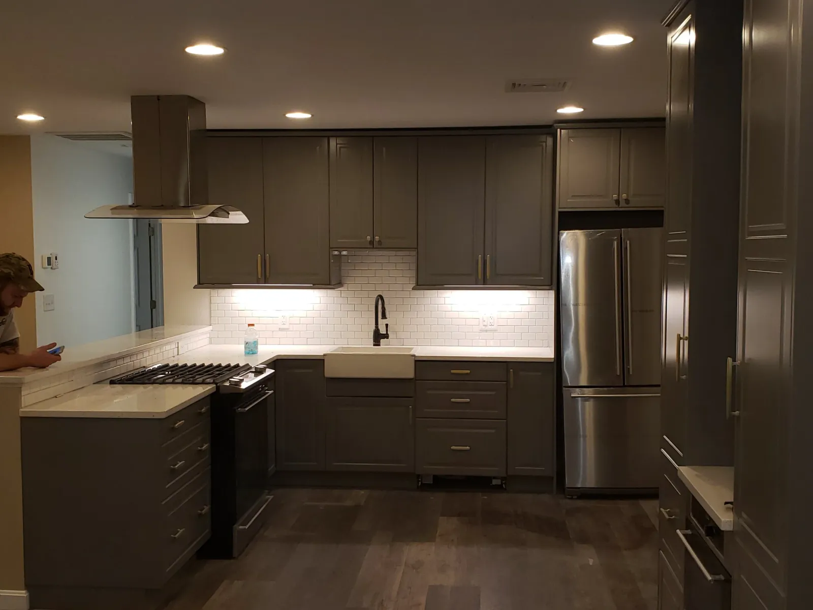 Modern kitchen with gray cabinets, stainless steel refrigerator, white countertops, subway tile backsplash, and a farmhouse sink.