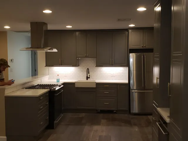 Modern kitchen with gray cabinets, stainless steel refrigerator, white countertops, subway tile backsplash, and a farmhouse sink.