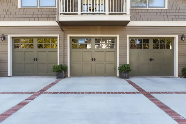 Three beige garage doors in a row with a concrete driveway and brick accents in front of a townhouse.