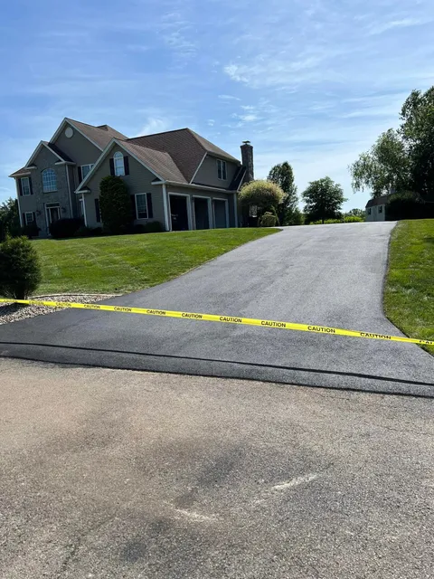 Yellow caution tape blocks a driveway leading to a large house on a sunny day