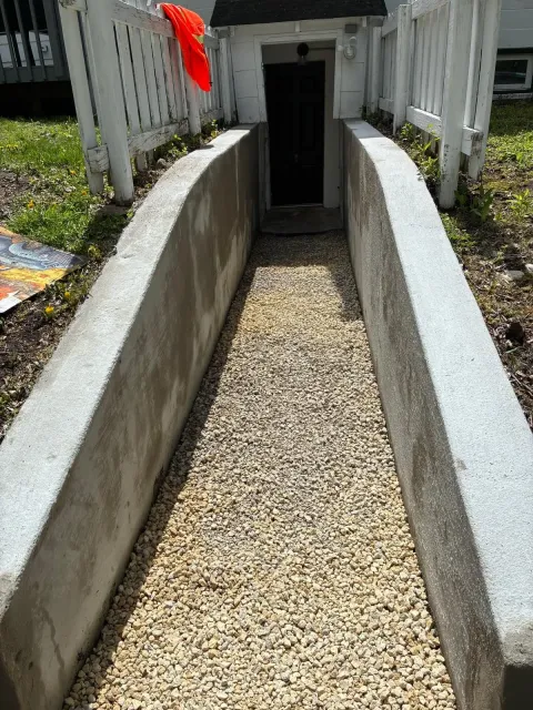 Gravel ramp between concrete walls leading to a doorway, with a red cloth hanging on the left.