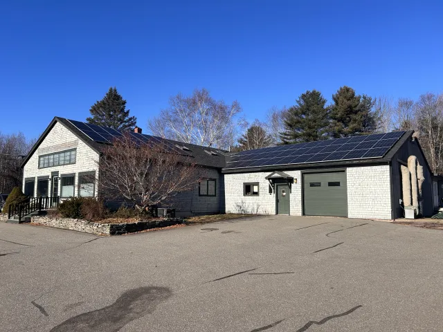 Gray house with solar panels on the roof, surrounded by trees and a paved driveway.
