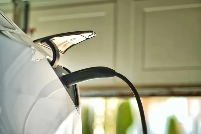 Electric vehicle charger plugged into a white car inside of a garage.