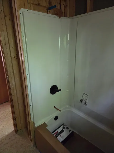 A new bathtub installed in an unfinished bathroom with exposed wooden wall frame and construction materials nearby.